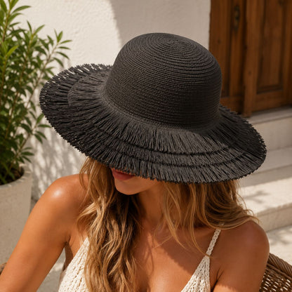 A woman wearing a wide-brimmed black woven sun hat with a frayed brim, seated outdoors in bright sunlight.