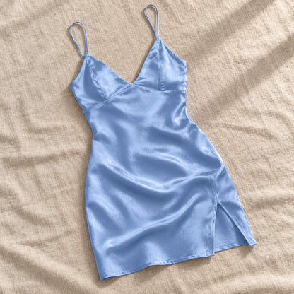Blue Amari Combs satin mini slip dress arranged diagonally on a beige fabric surface.